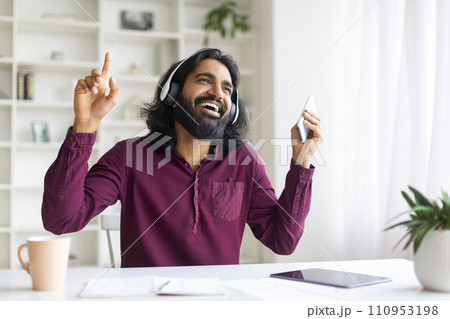 Cheerful Indian Man In Wireless Headphones Listening Music On Smartphone And Dancing Cheerful Indian Man In Wireless Headphones Listening Music On Smartphone And Dancing 110953198