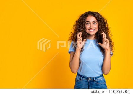 Woman with fingers crossed, hopeful look on yellow background Woman with fingers crossed, hopeful look on yellow background 110953200