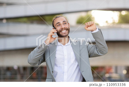 Joyful young businessman celebrating success during outdoor phone call 110953336