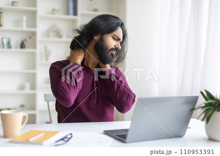 Tired Indian Freelancer Man With Neck Pain Sitting At Desk With Laptop 110953391