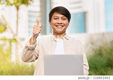 Cheerful young asian guy student using laptop outdoors Cheerful young asian guy student using laptop outdoors 110953401