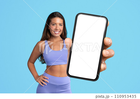 lady in fitwear showcasing large phone with empty screen, studio 110953435