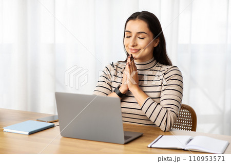 Positive young arab lady manager work at computer, make pray gesture, expect good news 110953571