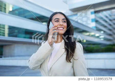 Happy latin entrepreneur woman talking on smartphone outside 110953579