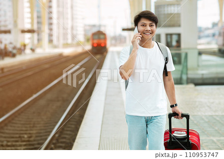 Happy guy tourist walking by train station, talking on phone 110953747