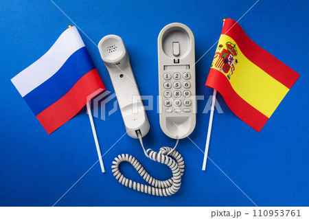 Old telephone and flags of Russia and Spain on a blue background, concept on the theme of telephone conversations between countries 110953761
