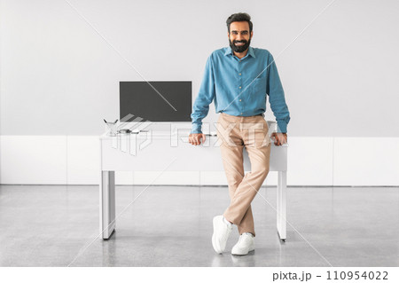 Confident indian man standing by office desk 110954022
