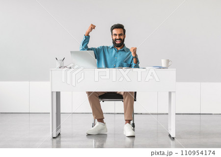 Joyful indian man celebrating success at desk Joyful indian man celebrating success at desk 110954174