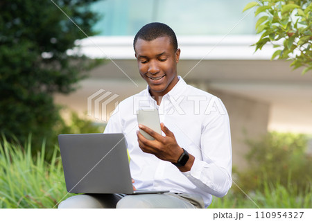 Modern Technologies For Business. Black Businessman Using Laptop And Smartphone Outdoors Modern Technologies For Business. Black Businessman Using Laptop And Smartphone Outdoors 110954327