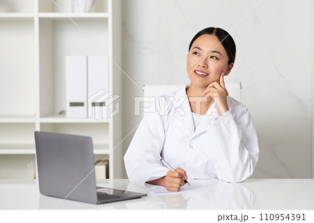 Medicine Concept. Pensive asian female doctor sitting at desk and taking notes Medicine Concept. Pensive asian female doctor sitting at desk and taking notes 110954391