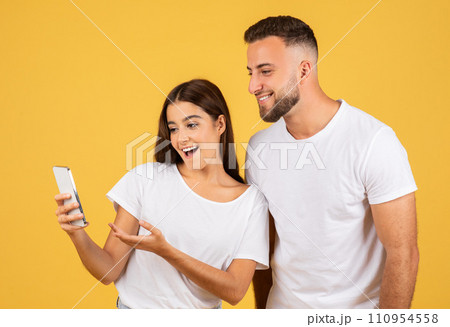 Happy shocked young european woman in casual show phone to man Happy shocked young european woman in casual show phone to man 110954558
