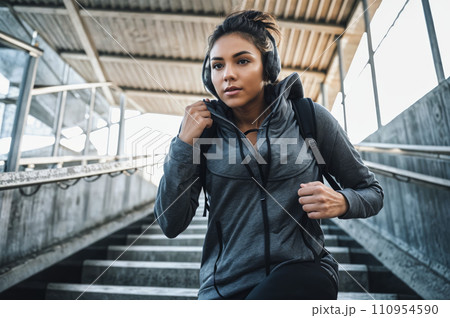 A women with headphone listen music in a grey hoodie and black backpack running down for concrete stairs. Concept healthy sport lifestyle. 110954590