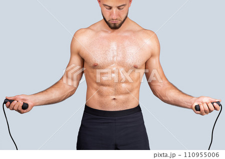 Focused sweat strong muscular millennial european man with beard, naked torso make exercises with skipping rope Focused sweat strong muscular millennial european man with beard, naked torso make exercises with skipping rope 110955006