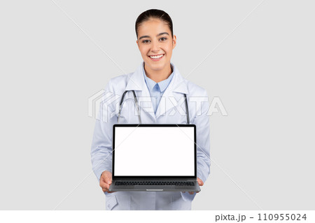 Cheerful caucasian young woman doctor in white coat show laptop computer with blank screen Cheerful caucasian young woman doctor in white coat show laptop computer with blank screen 110955024