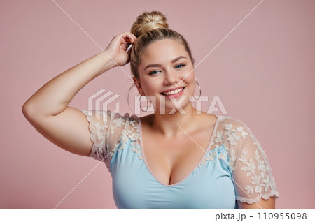 A woman with blonde hair tied in a bun, wearing a blue shirt with white lace details. She has hoop earrings and is smiling. Self-acceptance and body positivity concept. A woman with blonde hair tied in a bun, wearing a blue shirt with white lace details. She has hoop earrings and is smiling. Self-acceptance and body positivity concept. 110955098