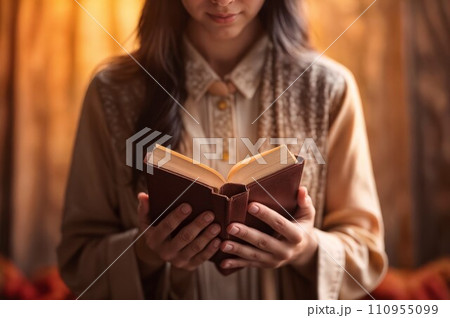 A woman with a light brown shirt holding a Bible book in front of her with both hands. A woman with a light brown shirt holding a Bible book in front of her with both hands. 110955099