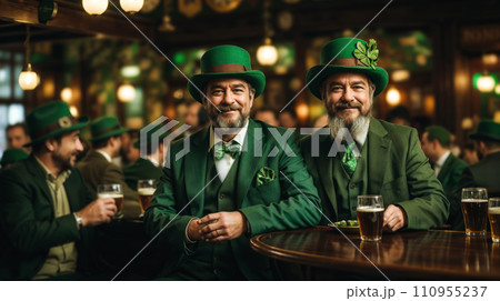 Two men dressed in green, with green hats and suits. They are sitting at a table in a pub with green shamrock decorations around them celebrating St. Patrick. Two men dressed in green, with green hats and suits. They are sitting at a table in a pub with green shamrock decorations around them celebrating St. Patrick. 110955237