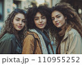 Three beautiful young women with curly hair standing next to each other on the street. Three beautiful young women with curly hair standing next to each other on the street. 110955252