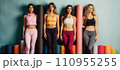 A group of women in sportswear stand in front of yoga mats in a variety of colors. 110955255