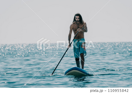 Man Sup Sea. Strong athletic man learns to paddle sup standing on board in open sea ocean on sunny day. Summer holiday vacation and travel concept. Aerial view. Slow motion 110955842