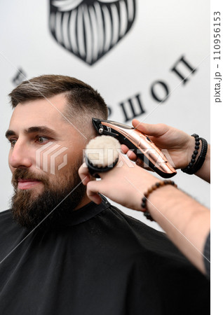 A barber cuts a man with a beard in a barber shop. Short haircut of the client with clipper. A barber cuts a man with a beard in a barber shop. Short haircut of the client with clipper. 110956153