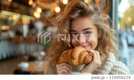 Young beautiful girl eating a large croissant in a Parisian cafe Young beautiful girl eating a large croissant in a Parisian cafe 110956218