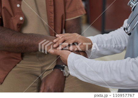 Unrecognizable female medical worker holding hand of her black patient expressing her moral support 110957767