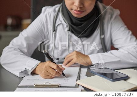 Unrecognizable young female doctor filling documents sitting at desk in hospital office 110957837