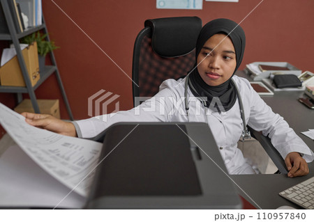 Young muslim doctor making copy of medical document sitting at her desk in office 110957840