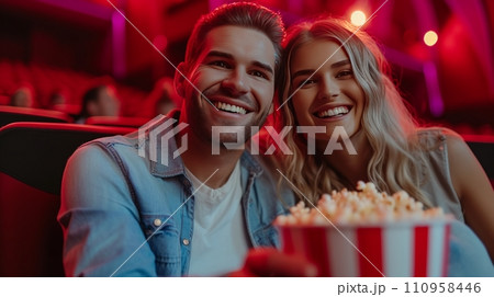Beautiful young couple sitting in a cinema with a big bucket of popcorn Beautiful young couple sitting in a cinema with a big bucket of popcorn 110958446
