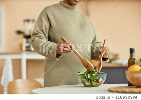 Cropped shot with focus on glass bowl with healthy vegetable salad and unrecognizable pregnant woman mixing ingredients with wooden stirring spoons Cropped shot with focus on glass bowl with healthy vegetable salad and unrecognizable pregnant woman mixing ingredients with wooden stirring spoons 110958584