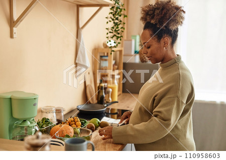 Side view of pregnant young African American woman preparing meal on kitchen table from fresh ingredients 110958603