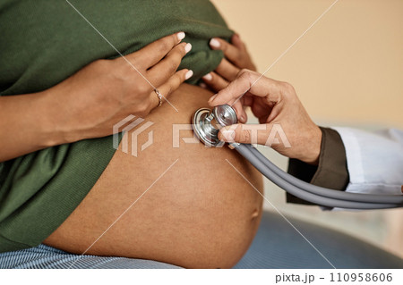 Close up shot of pregnant Black female patients round belly and unrecognizable obstetricians hand conducting auscultation Close up shot of pregnant Black female patients round belly and unrecognizable obstetricians hand conducting auscultation 110958606