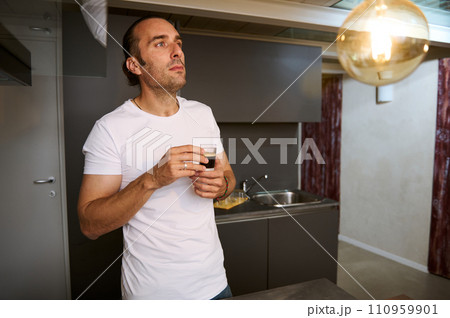 Contented young adult man holding cup of aroma arabica espresso coffee, enjoying warm beverage at home 110959901