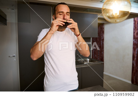 Handsome young man in white t-shirt, enjoying his morning coffee at home 110959902