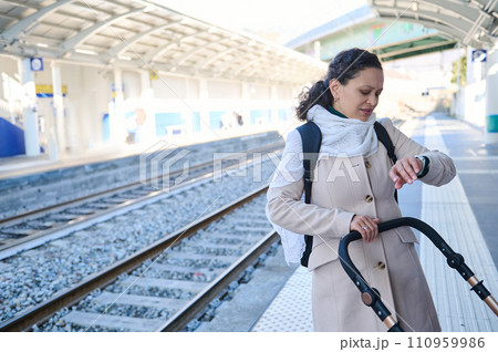 Young multi ethnic woman mother pushing baby stroller and checking time on wristwatch, feeling worried about train delay Young multi ethnic woman mother pushing baby stroller and checking time on wristwatch, feeling worried about train delay 110959986