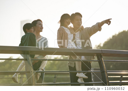asian family with two children standing on pedestrian bridge looking at view in city park at sunset asian family with two children standing on pedestrian bridge looking at view in city park at sunset 110960032