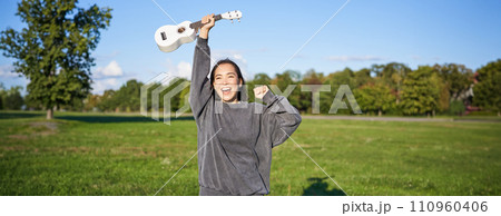 Positive beauty girl with ukulele, dancing and feeling freedom, looking excited, triumphing and celebrating Positive beauty girl with ukulele, dancing and feeling freedom, looking excited, triumphing and celebrating 110960406