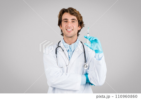 Smiling doctor with syringe ready for vaccination on gray background 110960860