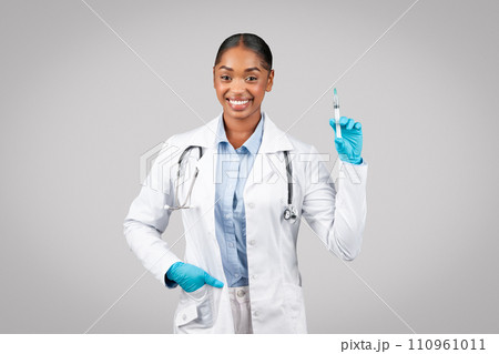 Positive millennial black woman doctor in white coat, protective gloves use syringe, recommendation vaccination 110961011
