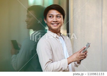 Young asian man with wireless earphones holding smart phone Young asian man with wireless earphones holding smart phone 110961133