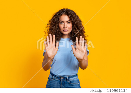 Curly-haired woman gesturing stop with hands on yellow background Curly-haired woman gesturing stop with hands on yellow background 110961134