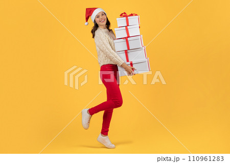 Happy lady posing with stack of Christmas presents, yellow backdrop 110961283