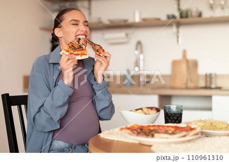 Joyful pregnant woman biting two pizza slices 110961310