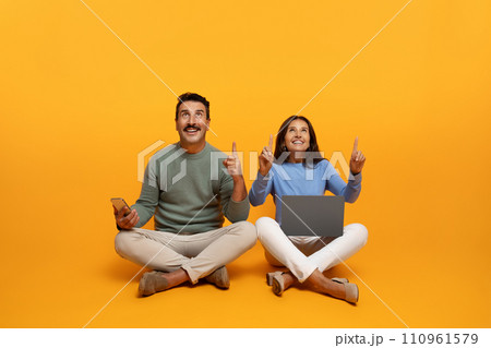 Glad inspired senior european husband and wife sit on floor with laptop, point finger up at free space 110961579