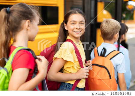 Portrait Of Smiling Girl With Backpack Boarding Yellow School Bus With Classmates 110961592