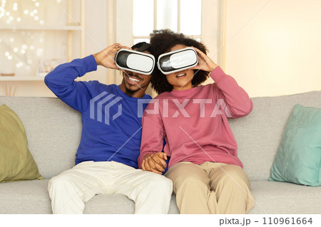 African American spouses wearing virtual reality headsets in living room African American spouses wearing virtual reality headsets in living room 110961664