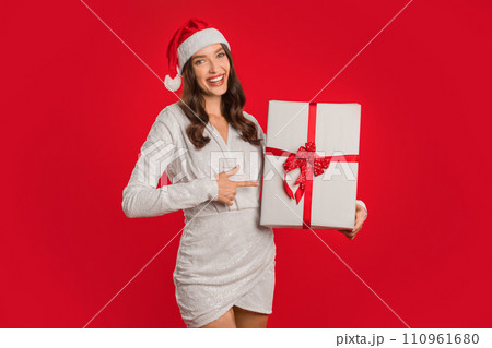 Joyful woman celebrates Christmas season pointing at wrapped gift, studio 110961680