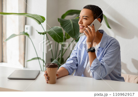 Happy young latin woman enjoy cup of coffee at table and call by smartphone with laptop in cafe Happy young latin woman enjoy cup of coffee at table and call by smartphone with laptop in cafe 110962917
