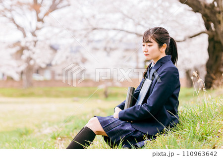 満開の桜の下に座る寂しい表情の高校生・女子高生（卒業・卒業生・悲しい・卒業証書） 110963642